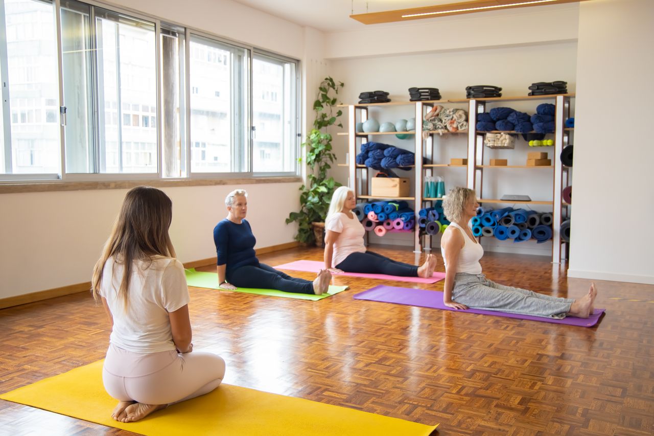 A diverse group of senior women practicing yoga indoors with mats.